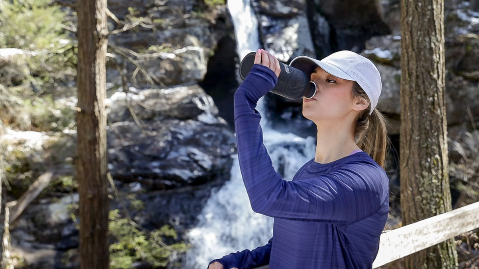 A woman drinks from a TrailHeads water bottle to hydrate during a hike