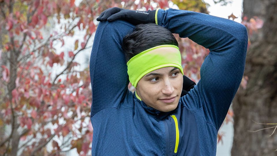 A man stretches wearing TrailHeads Power Stretch Gloves and a Hi Vis Yellow Headband