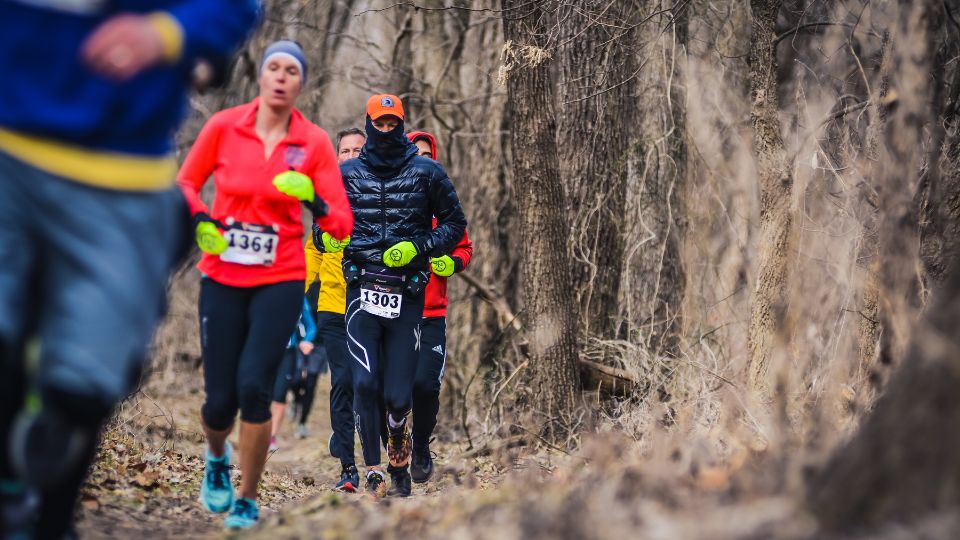 Runners on a woodsy path wear cold weather gear and accessories